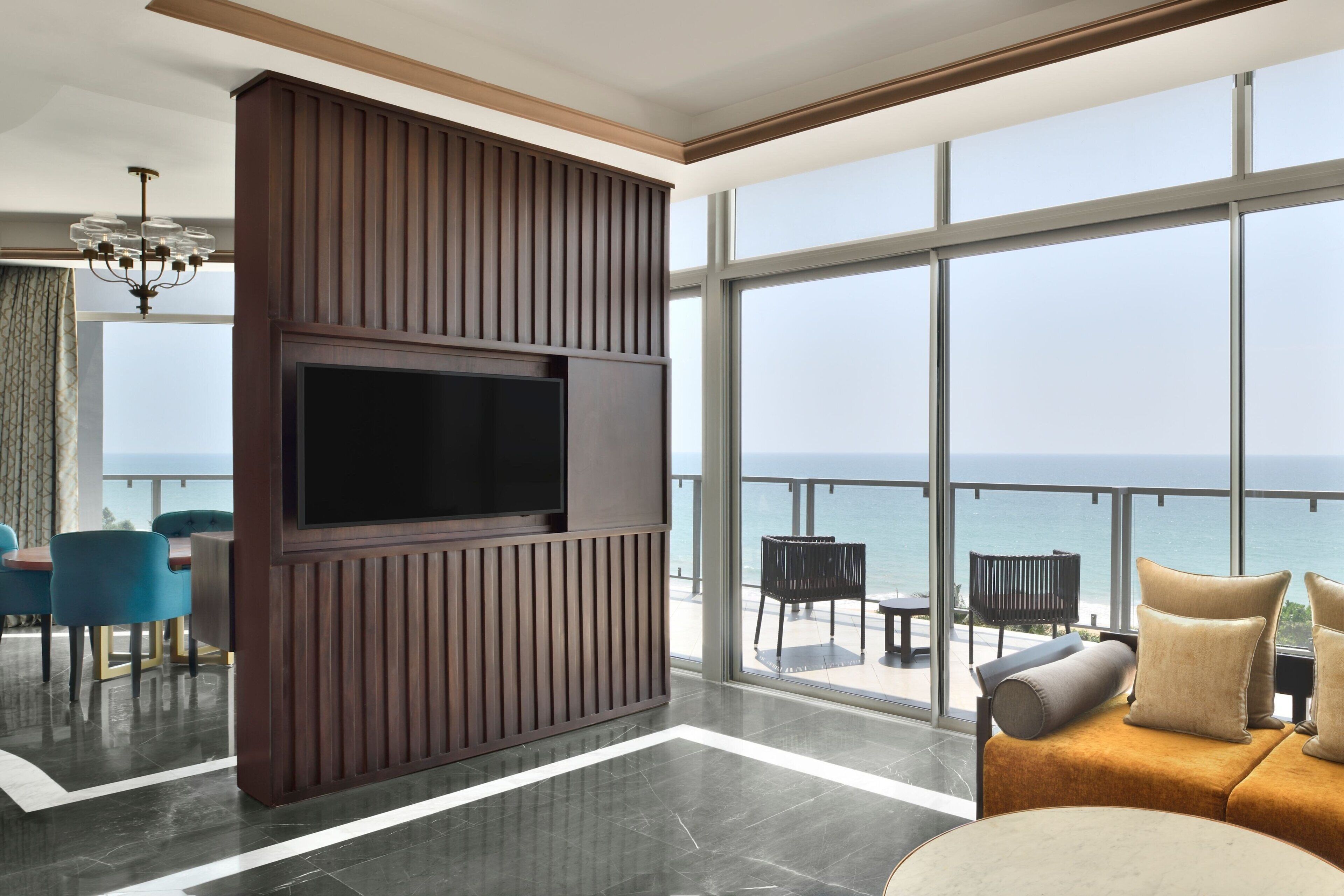 A modern living room with a large TV, a sofa, and a view of the ocean.