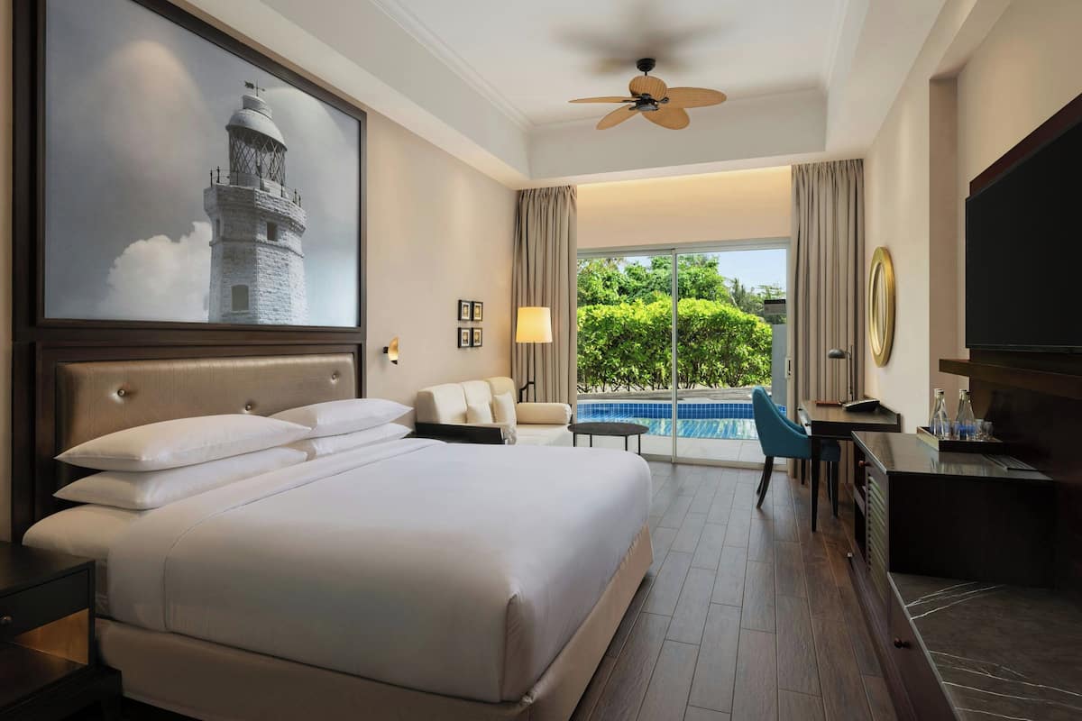 Ein Hotelzimmer mit einem großen Bett, einem Schreibtisch mit Fernseher, einem Deckenventilator und Blick auf einen Swimmingpool.