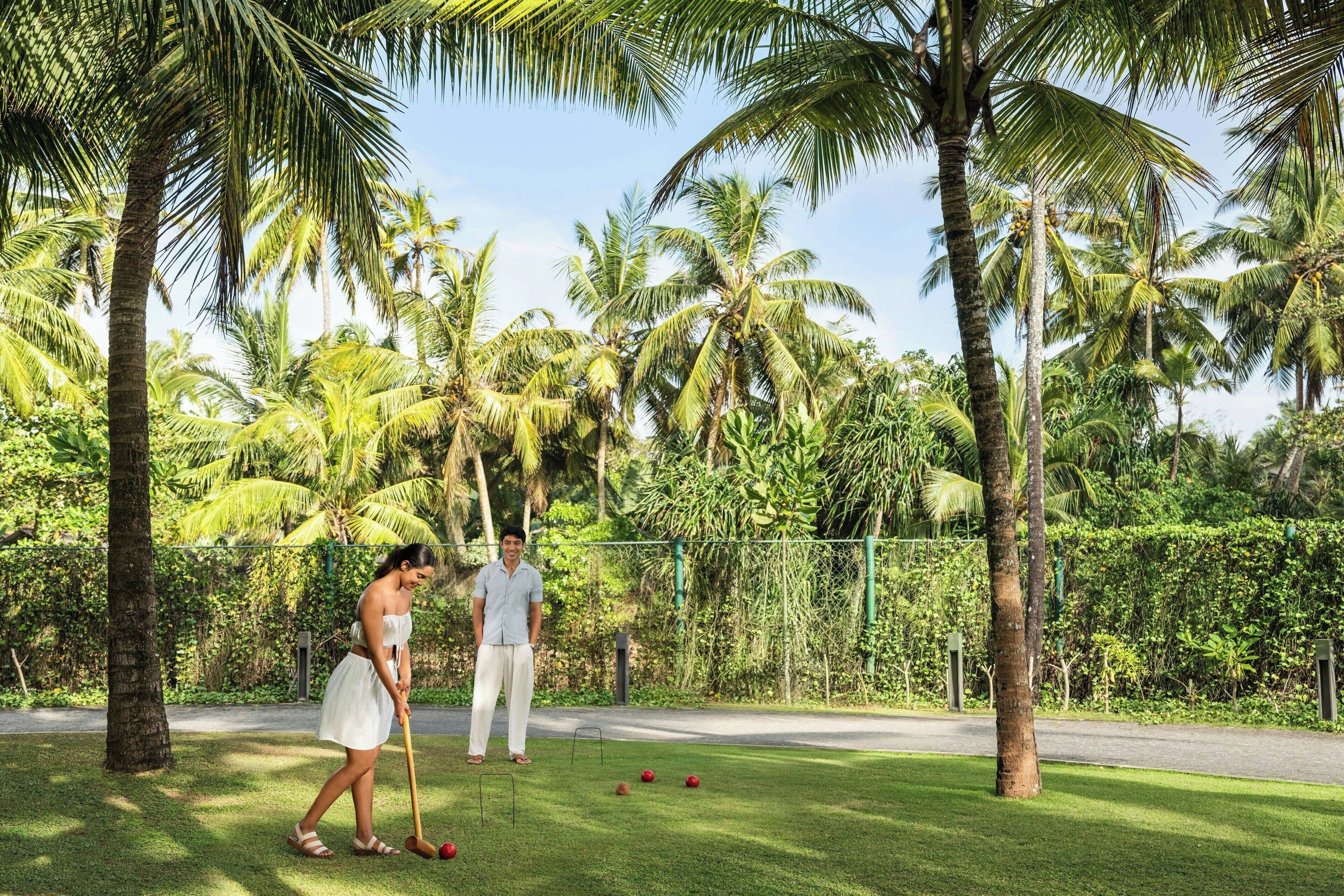 A lush garden with palm trees and a croquet field.