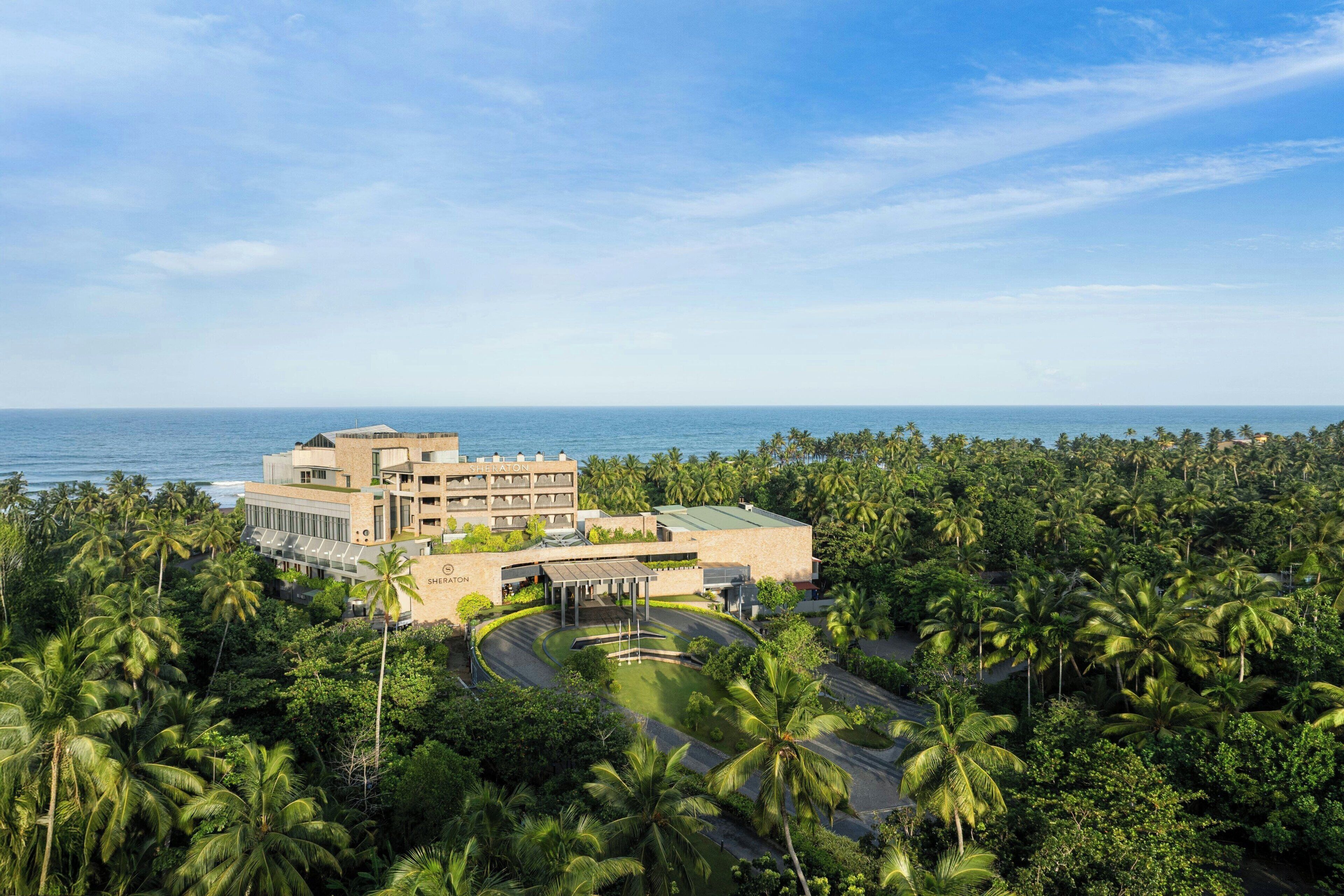A hotel with a view of the ocean, surrounded by palm trees.
