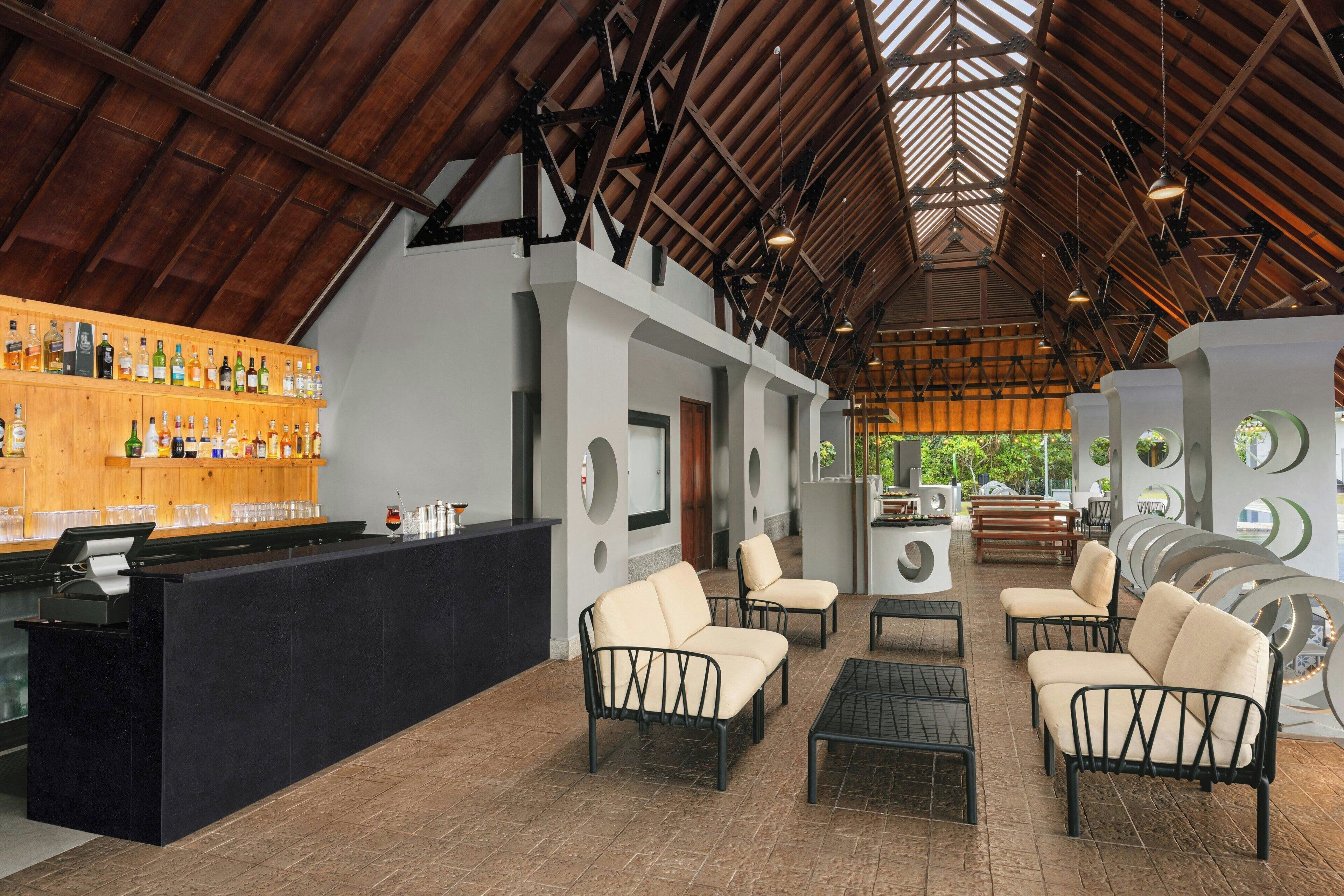 Amplia zona de bar con mostrador de madera y una variedad de botellas. Hay varias áreas de estar con sillas y mesas acolchadas.