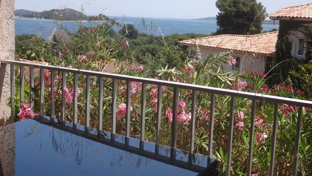 Een balkon met een hek dat uitkijkt over een kustlandschap met begroeiing en uitzicht op zee.