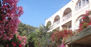A building with multiple balconies and arches, surrounded by lush greenery and flowering plants.