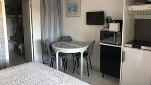 Een compacte kamer met een bed, een klein eettafeltje met stoelen, een kitchenette met een magnetron en een koelkast, en een televisie aan de muur.