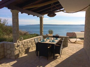 Enjoy al fresco dining with a view of the sea from this outdoor patio, featuring a stone table and chairs.