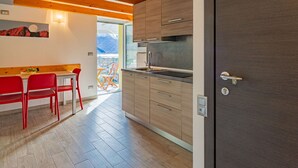 Une cuisine moderne avec des meubles en bois, un évier en acier inoxydable et une vue sur un balcon aménagé avec du mobilier d’extérieur.