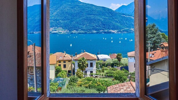 Une vue depuis une fenêtre donnant sur un lac où naviguent des voiliers, le tout entouré de bâtiments aux toits recouverts de tuiles rouges.
