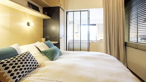 Een moderne slaapkamer met een groot bed, een nachtkastje, een kledingkast en uitzicht buiten door een raam met gordijnen.