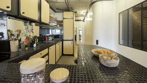 Een keuken met een zwart betegelde spatwand, houten kastjes en een aanrecht met verschillende keukenbenodigdheden.
