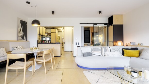 Een moderne woonkamer met een witte bank, een eettafel met stoelen, en een keuken op de achtergrond.