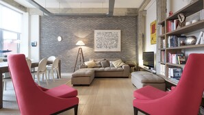 Un soggiorno moderno con un divano componibile, poltrone rosse, una libreria e un grande quadro astratto appeso al muro.