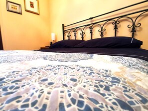 Ein Bett mit gemustertem Bettbezug, einem schwarzen Metall-Kopfstück und zwei gerahmten Bildern an der Wand.