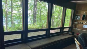 Une pièce dotée d’une grande fenêtre donnant sur une forêt, d’un banc intégré et d’une bibliothèque.