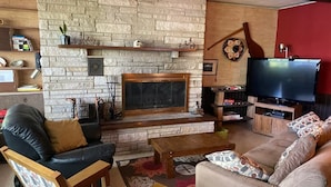 Un salon avec une cheminée en pierre, des canapés en cuir, une table basse en bois et un téléviseur.