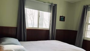 Un lit bien fait, avec une couette blanche et des oreillers, une fenêtre avec des rideaux et un petit tableau accroché au mur.