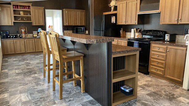 A kitchen with wooden cabinets, a granite countertop, a black refrigerator, a microwave, and a stove. - Texas Ranch House on 10 acres near Lake Ray Roberts! (Pilot Point)