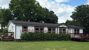 A single-story building with a porch, surrounded by a well-maintained lawn and trees. - Texas Ranch House on 10 acres near Lake Ray Roberts! (Pilot Point)