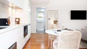 A modern kitchen with white cabinetry, a dining area with wicker chairs, and a flat-screen TV mounted on the wall. - Modern and Cosy Inner West Apartment (Lewisham)