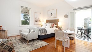 A bedroom with a bed, a sitting area with a chair and a table, and a view of the outdoors. - Modern and Cosy Inner West Apartment (Lewisham)