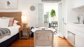 A compact hotel room with a bed, bedside table, lamp, and a dining area with chairs and a table. - Modern and Cosy Inner West Apartment (Lewisham)