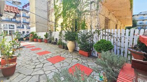 A courtyard with stone flooring, potted plants, a white picket fence, and a statue. - Hotel Exarhos (Katerini)