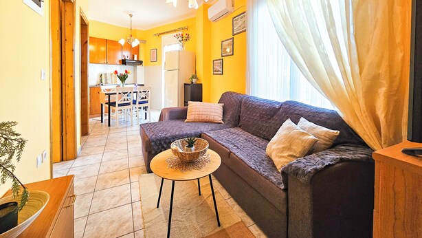 A living room with a sofa, a small round table, and a kitchen area in the background. - Hotel Exarhos (Katerini)