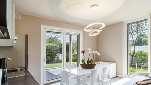 Una cocina moderna con horno empotrado, comedor con sillas blancas y vistas al exterior.