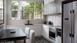 A modern kitchen with white cabinets, a built-in oven, a stainless steel refrigerator, and a window with a view of greenery.