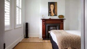 A bedroom with a bed, a fireplace, a painting, and a window with blinds.