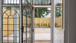 A view through a glass door with a metal grid, leading to a wooden fence and a small garden with plants.