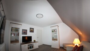 A modern living room with a flat-screen TV, built-in shelving, a sofa, and a lamp. - Welcome to the Trude house (Wulmeringhausen)