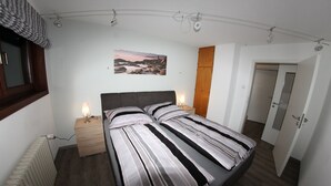 A bedroom with a bed, bedside lamps, a wooden nightstand, a radiator, a wall-mounted picture, and a door. - Welcome to the Trude house (Wulmeringhausen)
