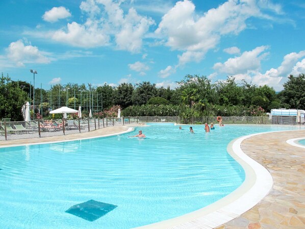 Une grande piscine extérieure à bords incurvés, entourée de chaises longues et de parasols, et dotée d’une terrasse en pierre.