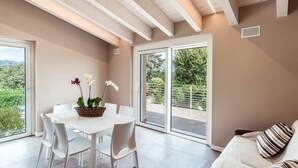A modern dining area with a white table and chairs, a basket of flowers, and a sliding glass door leading to an outdoor patio.