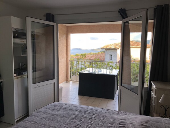 Une chambre avec un lit, une petite table et un balcon d’où l’on peut admirer une maison et des montagnes.