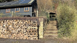 A rustic cabin with a stone wall, wooden steps, and a solar panel roof. - Rose Lodge, Eco Lodge with Hot Tub (Langport)