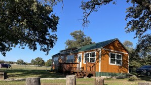 Een houten chalet met een groen dak, omringd door een omheind weiland en bomen.