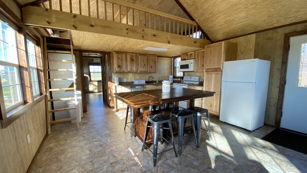 Een ruime keuken met houten kastjes, een groot eiland met barstoelen en een koelkast.