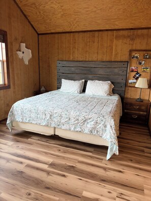 Un dormitorio con cabecera de madera, cama con colcha floral, mesita de noche con lámpara y pared decorada con un mapa de madera.