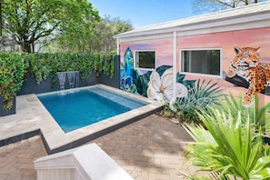 Piscina com um mural de um leopardo e flores, cercada por vegetação e um terraço de tijolos.