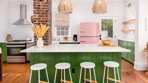 Eine moderne Küche mit grünen Schränken, einem pinken Kühlschrank und einer zentralen Kochinsel mit Barhocker.