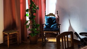 A room with a dining table, chairs, a potted plant, a rocking chair, and a window with curtains. - RURAL HOUSE TO ENJOY NATURE (Medina-Sidonia)