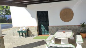 A patio area with a stone wall, a green door, a round woven mat, and a table with a green mat. - RURAL HOUSE TO ENJOY NATURE (Medina-Sidonia)