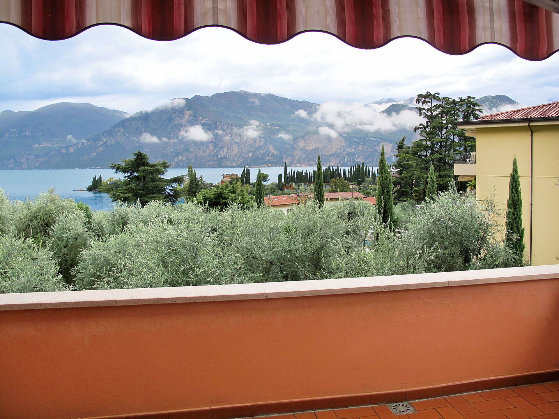 A balcony with a view of a lake, mountains, and a building with a red roof.