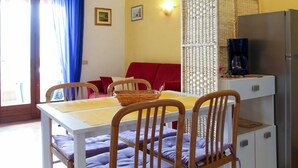A compact living space with a dining table, chairs, a sofa, a refrigerator, and a coffee maker. - Cosy apartment for 3 guests with WIFI, TV, balcony and pets allowed (Malcesine)