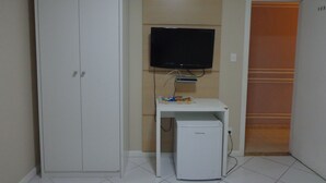 Ein Zimmer mit einem weißen Kleiderschrank, einer kleinen weißen Vorratskammer mit einem darüber montierten Fernseher und einem Kühlschrank.