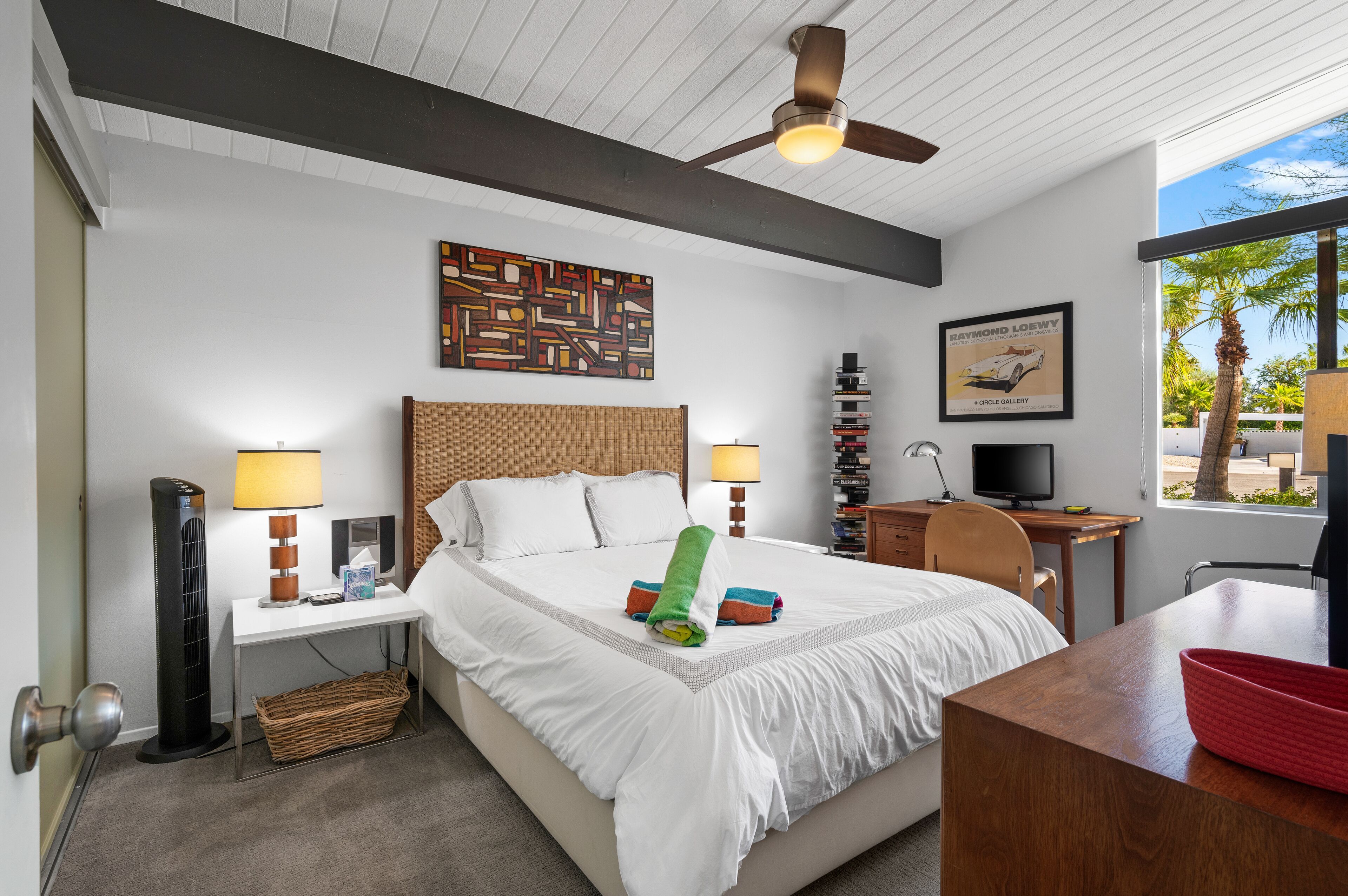 A hotel room with a bed, desk, chair, and a ceiling fan.