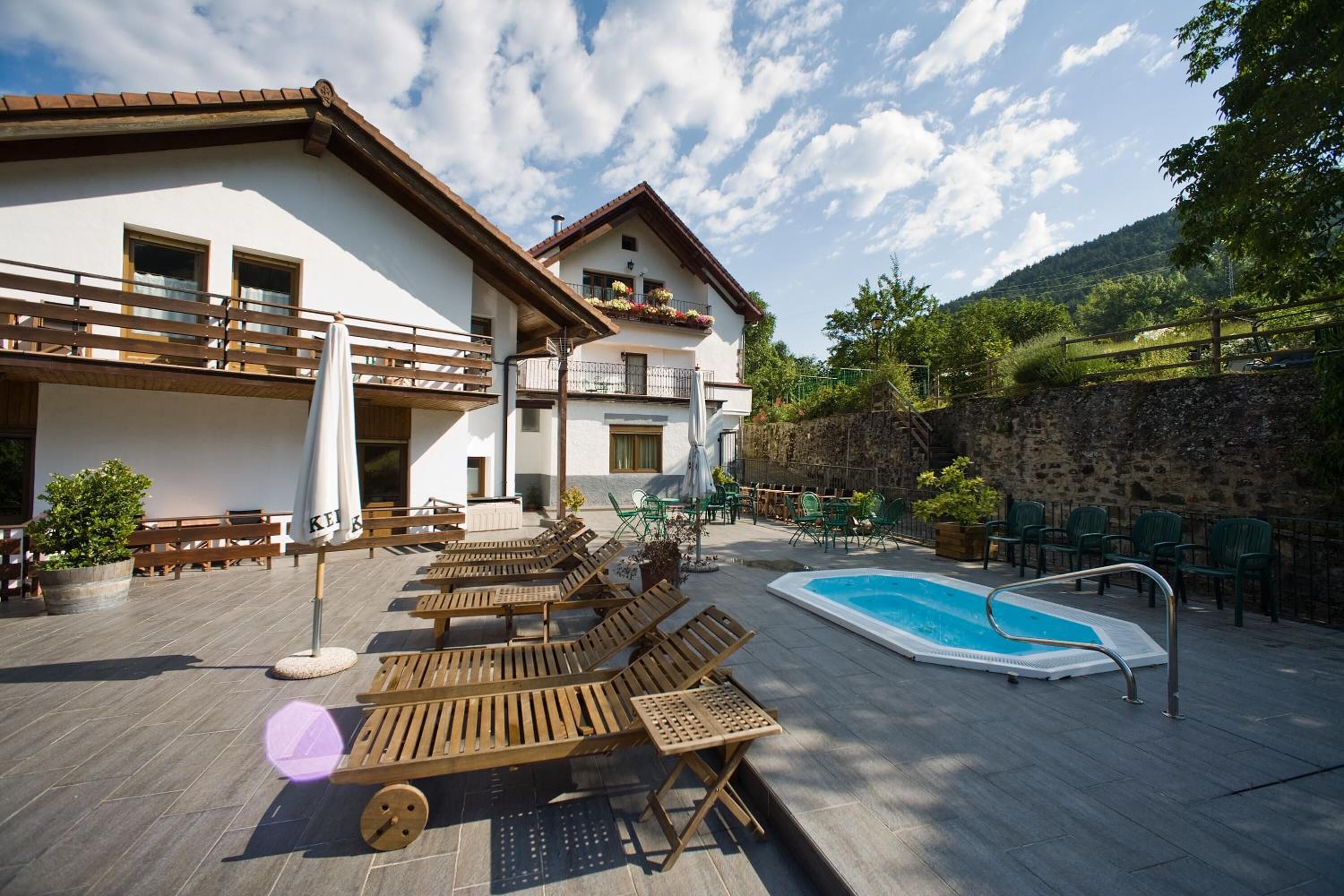 A poolside area with wooden loungers, a swimming pool, and outdoor seating.