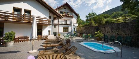 A poolside area with wooden loungers, a swimming pool, and outdoor seating.