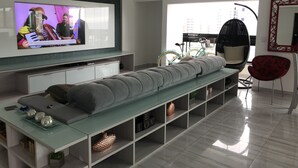 A modern living room with a flat-screen TV, a sofa, a glass coffee table, and a red chair. - COMPLETE LEISURE COVERAGE  (Praia Grande)